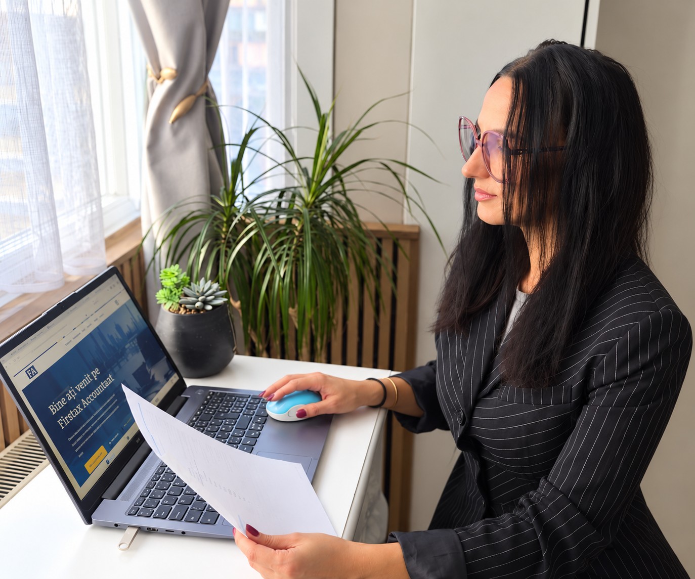 Cristina Mihaescu de la Firstax Accountant lucrând la birou, cu un laptop și un document în mână